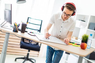 Gözlüklü ve kulaklıklı genç bir adam manyetik tahtaya bir işaret çizer..