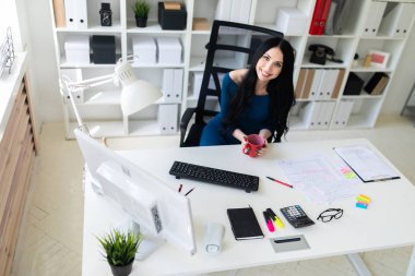 Genç bir kız ofiste masada oturur ve kırmızı bir fincan elinde tutan.