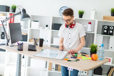 Gözlüklü genç bir adam bir bilgisayar masası duruyor. Genç bir adam bir işaretleyici manyetik bir tahtaya çizer. Çocuklar kulaklık boynuna asmak.