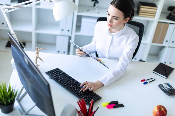 Una joven en la oficina tiene un bolígrafo en la mano y trabaja con documentos y una computadora . — Foto de Stock