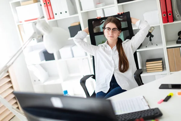 En ung flicka sitter vid ett bord på kontoret, lägga händerna bakom huvudet och titta på skärmen. — Stockfoto