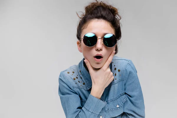 Jonge brunette meisje in ronde bril. Haren worden verzameld in een broodje. Het meisje stak haar hand op haar kin. — Stockfoto