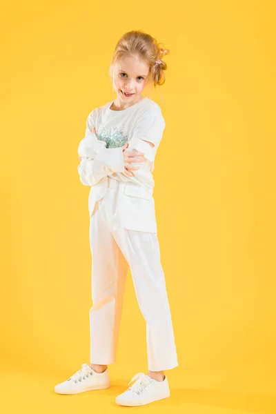 Une adolescente en vêtements blancs posant sur un fond jaune. La fille a baissé sa veste à ses coudes. — Photo