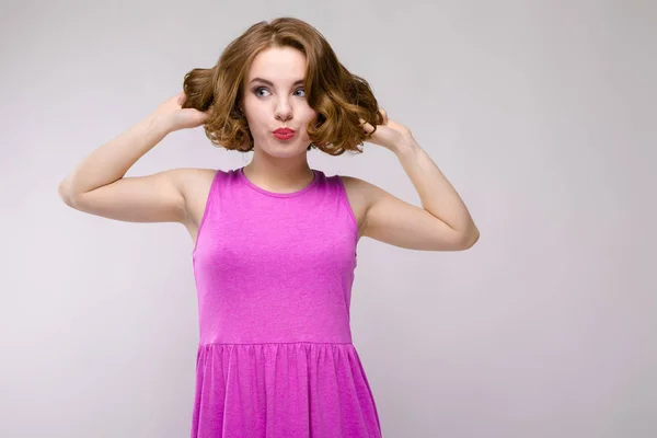 Charmante junge Mädchen in rosa Kleid auf grauem Hintergrund. ein junges Mädchen hält ihr Haar in den Händen — Stockfoto