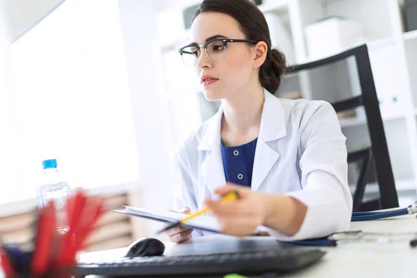 Una bella ragazza vestita di bianco è seduta su una scrivania con documenti e una penna in mano. Foto con profondità di campo, focus sulla ragazza . — Foto Stock