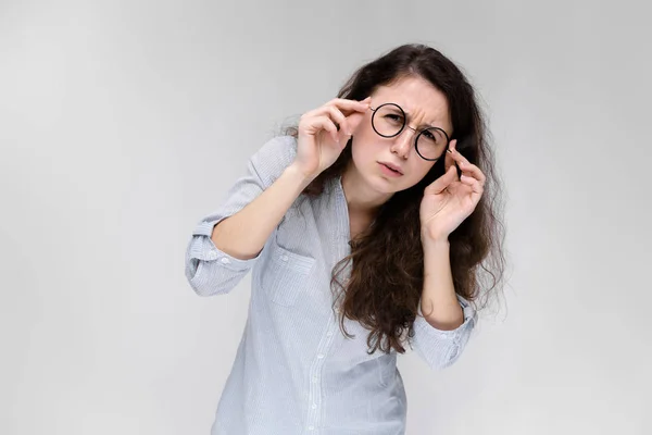 Retrato de una joven con gafas. Hermosa joven sobre un fondo gris. Una joven con una blusa clara y pantalones oscuros . — Foto de Stock