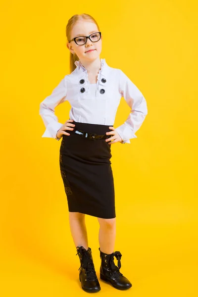 Menina com cabelo vermelho em um fundo amarelo. Uma menina encantadora em óculos transparentes colocar as mãos em seus quadris . — Fotografia de Stock