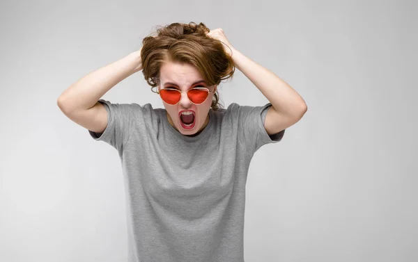 Encantadora joven con una camiseta gris sobre un fondo gris. Chica feliz en gafas rojas — Foto de Stock