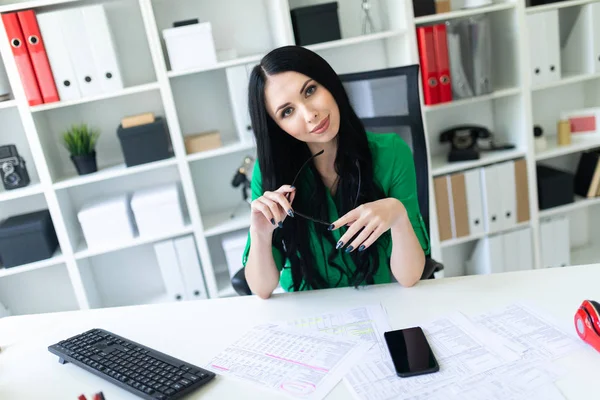 Ein junges Mädchen sitzt im Büro am Tisch und hält eine Brille in den Händen. — Stockfoto