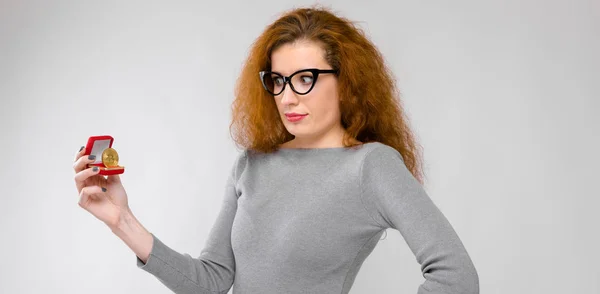 Retrato de bela ruiva mulher jovem surpreso em roupas cinza em óculos olhando em bitcoin como conceito criptomoeda — Fotografia de Stock
