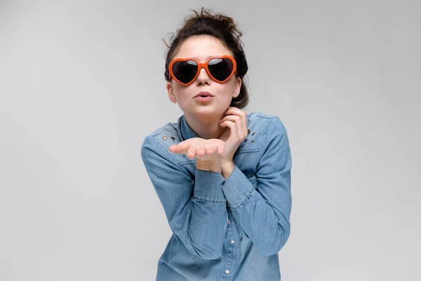 Junges brünettes Mädchen mit Brille in Form eines Herzens. Die Haare sind zu einem Dutt zusammengebunden. das Mädchen schickt einen Luftkuss. — Stockfoto