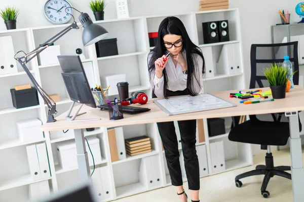 Genç bir kız bir bilgisayar masası duruyor ve bir işaretleyici manyetik bir tahtaya çizer.