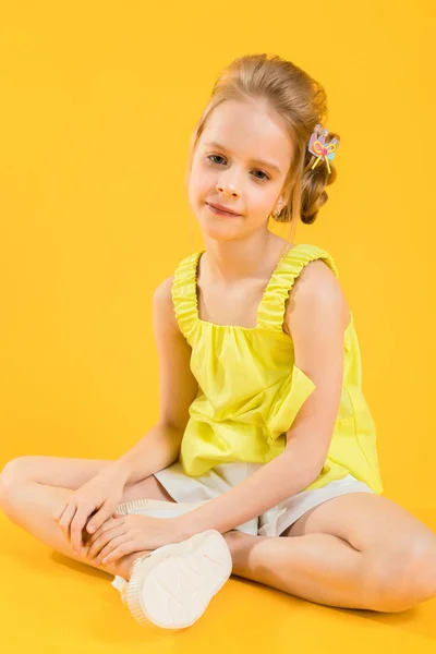 Uma adolescente está sentada em um fundo amarelo . — Fotografia de Stock