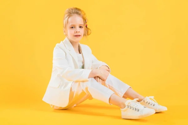 Ein junges Mädchen in weißen Kleidern sitzt und streckt ihre Beine vor einem gelben Hintergrund. — Stockfoto