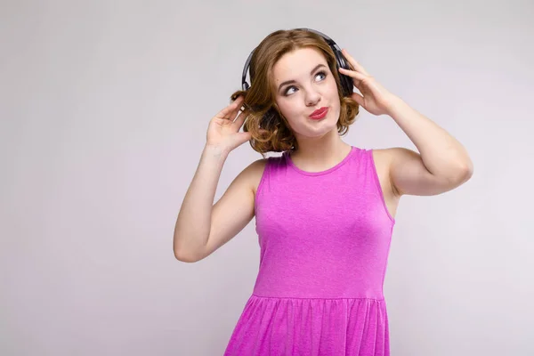 Encantadora joven en vestido rosa sobre fondo gris. Chica joven con auriculares sonriendo — Foto de Stock