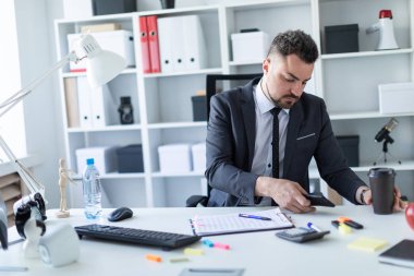 Bir adam bir telefon ve bir bardak kahve elinde tutan masada, ofisinde oturuyor.