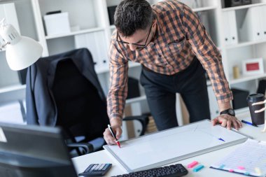 Bir adam ofiste masanın yanında duruyor ve bir işaretleyici manyetik tahtaya çizer.