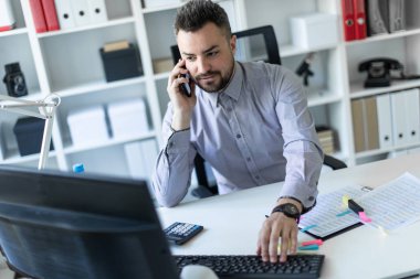 Genç bir adam, telefonda ve bilgisayarda çalışan oturuyor.