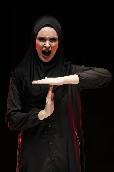 Retrato de una hermosa mujer musulmana asustada y desesperada con hiyab negro mostrando una señal de stop sobre un fondo negro — Foto de Stock