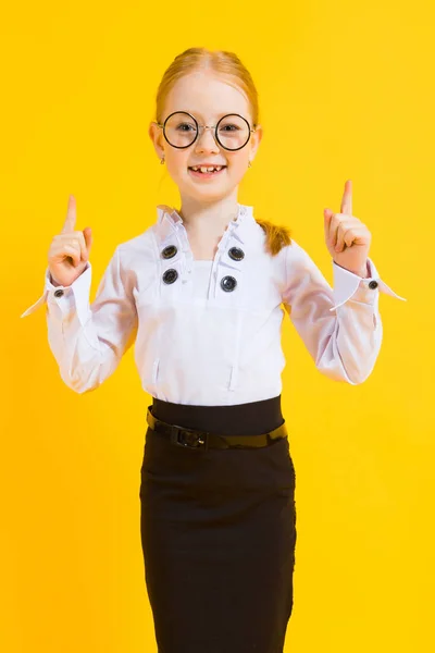 Mädchen mit roten Haaren auf gelbem Hintergrund. ein charmantes Mädchen mit durchsichtiger Brille zeigt ihre Finger nach oben. — Stockfoto