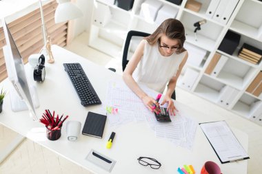 Ofiste genç bir kızın elinde pembe bir işaretçi tutar ve Hesap makinesinde sayar.