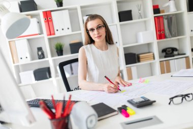 Güzel genç kız ofiste masada oturmuş, elinde kalem tutan ve belgeleri doldurma.