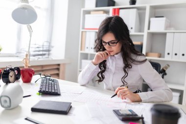Genç bir kız ofis masada oturur, onun elinde bir kalem tutan ve belgeleri görünüyor.