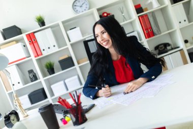 Güzel genç kız ofiste belgelerle masada çalışıyor ve bir kalem elinde tutuyor.