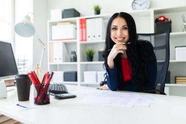 Güzel bir genç kız ofiste masada oturur ve onun elinde kalem tutan.