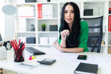 Genç bir kız ofiste masada oturur ve gözlük onun elinde tutan.