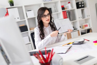 Güzel bir genç kız ofiste bir masada oturan ve bir kalem belgedeki bilgi işaret.