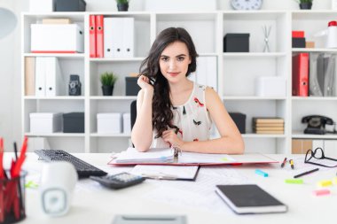 Güzel bir genç kız ofis masada oturur, saçları onun elinde tutan ve düz görünüyor.