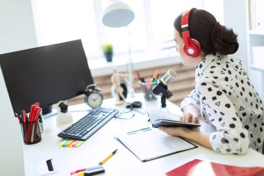 Güzel genç kız kulaklık ve bir not defteri ofiste masada oturur ve mikrofona konuşur.