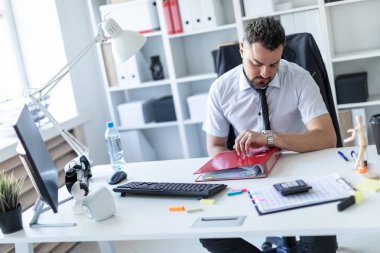 Bir adam ofiste bir masada oturur ve kol saati görünüyor.