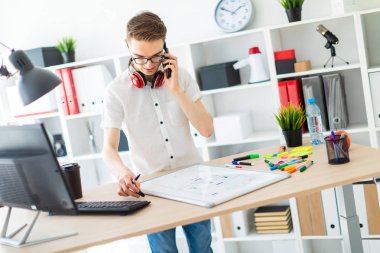 Gözlüklü genç bir adam bir bilgisayar masası duruyor ve telefonda konuşuyor. Önce onu bir manyetik kurulu ve işaretleri yatıyor. Çocuklar kulaklık boynuna asmak.