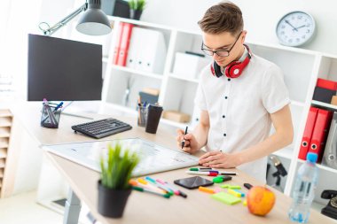 Gözlüklü genç bir adam bir bilgisayar masası duruyor. Genç bir adam bir işaretleyici manyetik bir tahtaya çizer. Çocuklar kulaklık boynuna asmak.