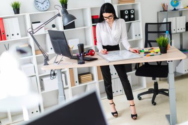 Genç bir kız bir bilgisayar masası duruyor ve bir işaretleyici manyetik bir tahtaya çizer.