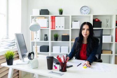 Güzel bir genç kız ofiste beyaz bir masada bir sandalyede oturur ve sarı bir marker ile belgelerdeki önemli noktaları vurgular.