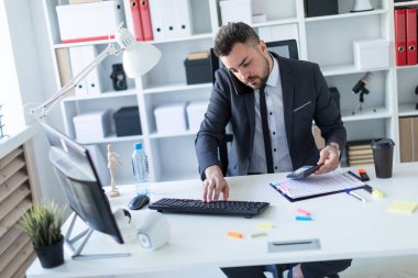 Adam bir hesap makinesi elinde tutan masasında ofisinde oturuyor, onun omuz ile belgili tanımlık telefon çekmek ve klavyede yazdırır.