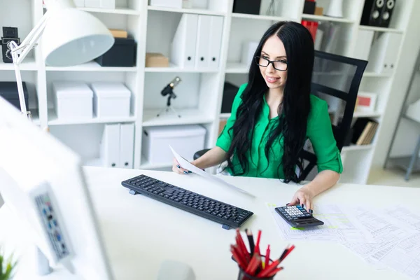 Девушка в очках работает в офисе с компьютером, калькулятором и документами . — стоковое фото