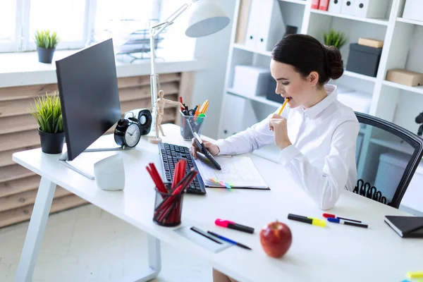 Una joven en la oficina tiene un bolígrafo en la boca y trabaja con una calculadora, documentos y una computadora . — Foto de Stock