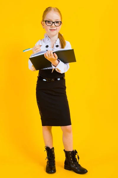 Ragazza con i capelli rossi su sfondo giallo. Una ragazza affascinante in occhiali trasparenti scrive una penna nel suo taccuino . — Foto Stock