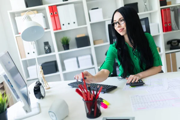 Een jong meisje in glazen werkt in het kantoor met een computer, een rekenmachine en documenten. — Stockfoto