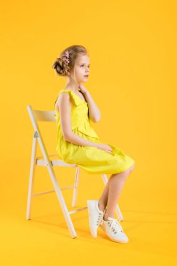Bir kız sarı bir arka plan üzerinde beyaz bir sandalyede oturuyor.