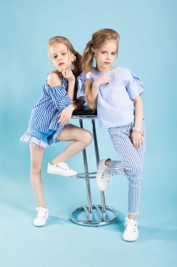 Kızlar ikizler mavi elbise bir barın yakınında poz ışık mavi bir arka plan üzerinde tabure.