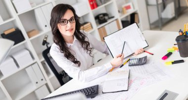 Güzel bir genç kız ofiste bir masada oturan ve bir kalem belgedeki bilgi işaret.