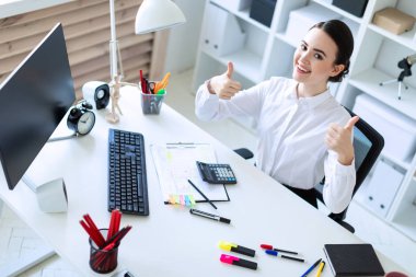 Ofiste genç bir kız bir masada oturuyor, belgeleri ile çalışır ve bir sınıf işaret gösterir.