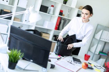 Bir genç kız ofiste masanın yanında duruyor ve çantaya şey koyar.