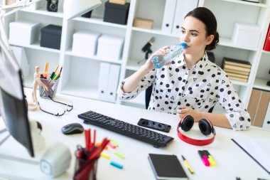 Güzel bir genç kız ofiste bir masada oturur ve bir şişe suyu içer.