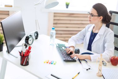 Beyaz bir elbise içinde güzel bir genç kız masada oturan ve klavyede yazarak.